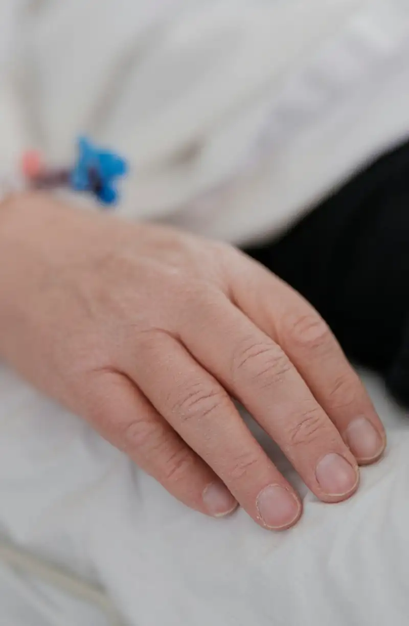 Mano de un paciente en una cama de hospital, con un catéter en la muñeca